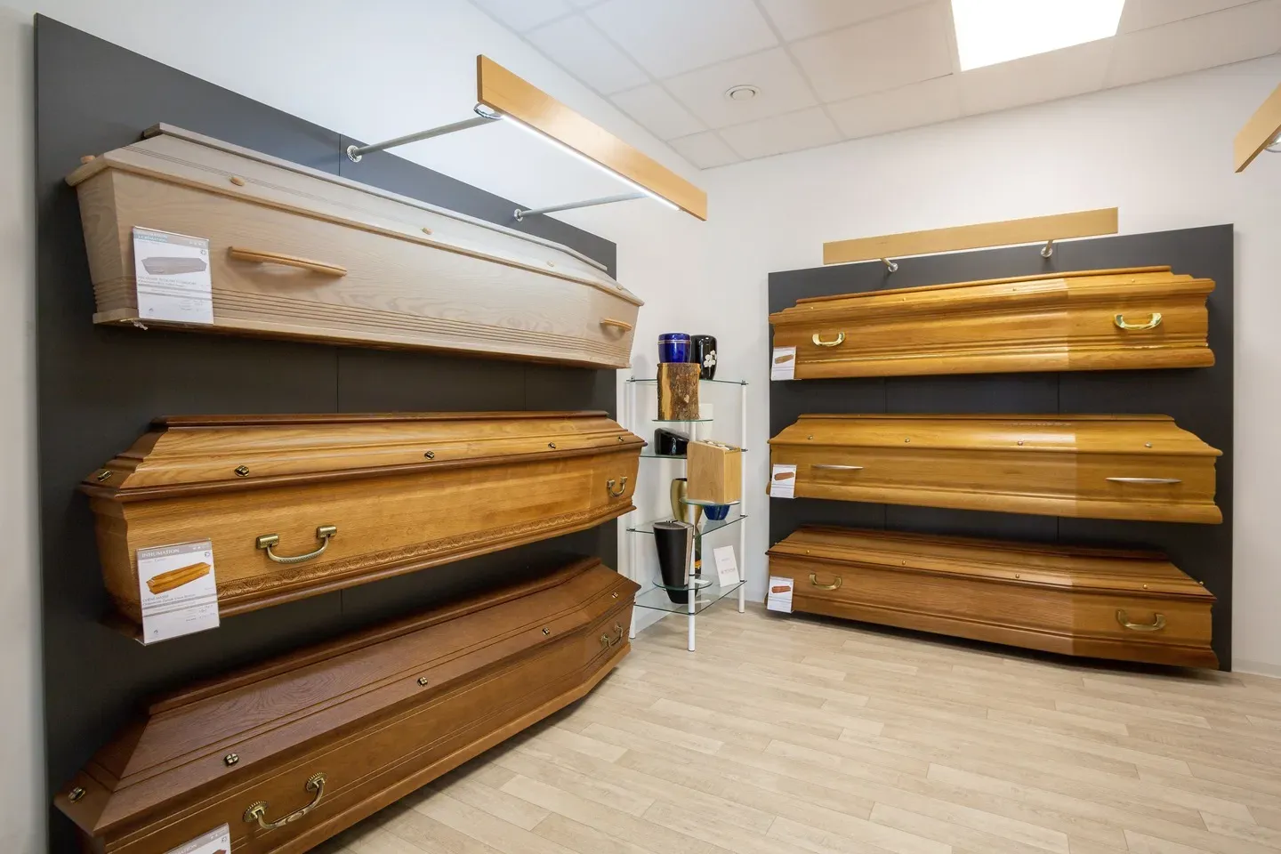 Exposition de cercueils en bois de différentes essences dans un showroom.